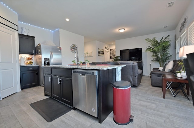 kitchen featuring visible vents, an island with sink, open floor plan, light stone countertops, and stainless steel appliances