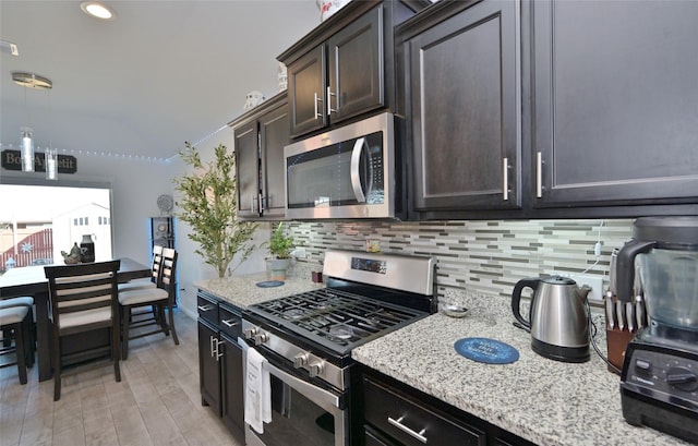 kitchen with dark brown cabinetry, hanging light fixtures, appliances with stainless steel finishes, light stone countertops, and tasteful backsplash