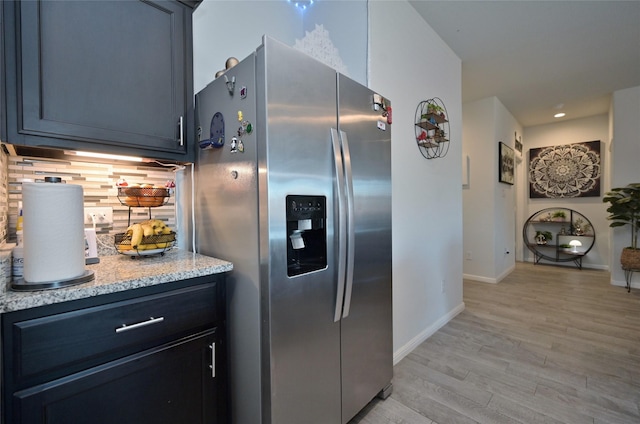 kitchen featuring tasteful backsplash, stainless steel fridge with ice dispenser, light wood-style floors, light stone countertops, and baseboards