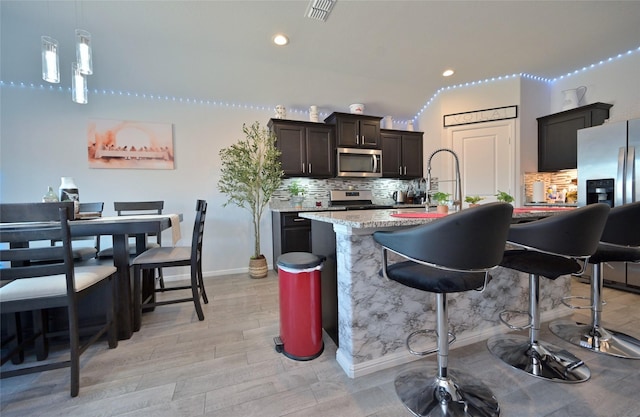 kitchen featuring a kitchen island with sink, visible vents, a kitchen breakfast bar, appliances with stainless steel finishes, and tasteful backsplash