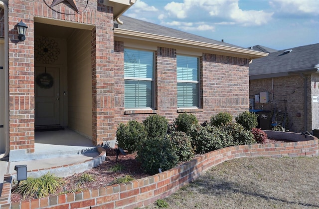 doorway to property featuring brick siding and a shingled roof