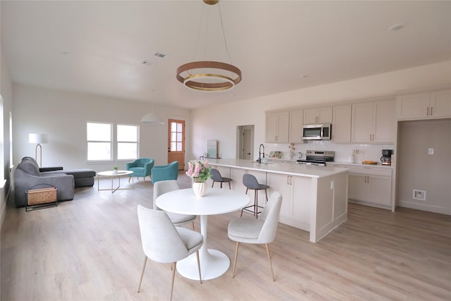 kitchen with a center island with sink, appliances with stainless steel finishes, open floor plan, decorative light fixtures, and light countertops