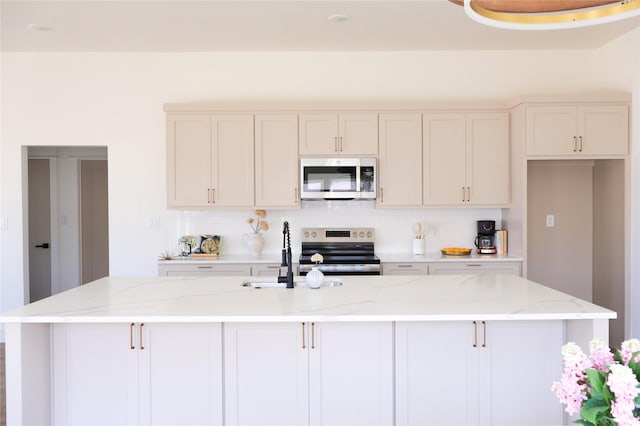 kitchen featuring appliances with stainless steel finishes, a kitchen island with sink, and light stone countertops