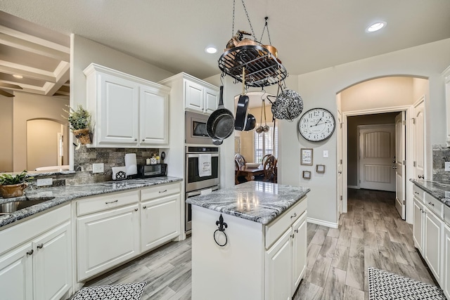 kitchen with arched walkways, tasteful backsplash, dark stone counters, and white cabinets