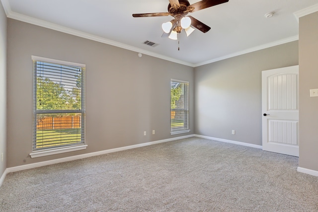 carpeted spare room with visible vents, crown molding, baseboards, and ceiling fan