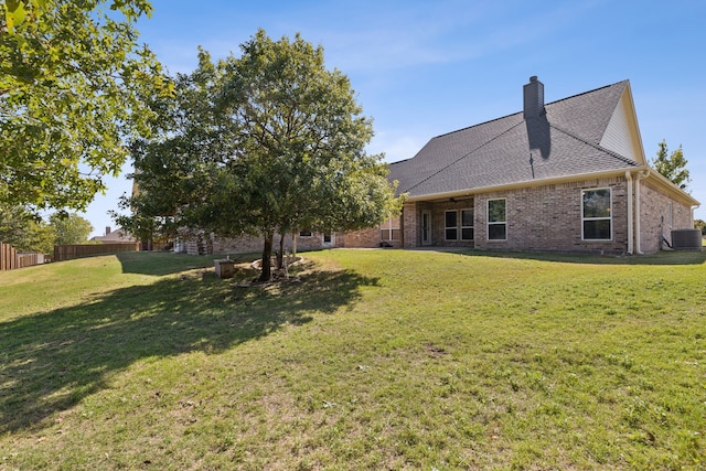 exterior space featuring central air condition unit, brick siding, fence, a yard, and a chimney