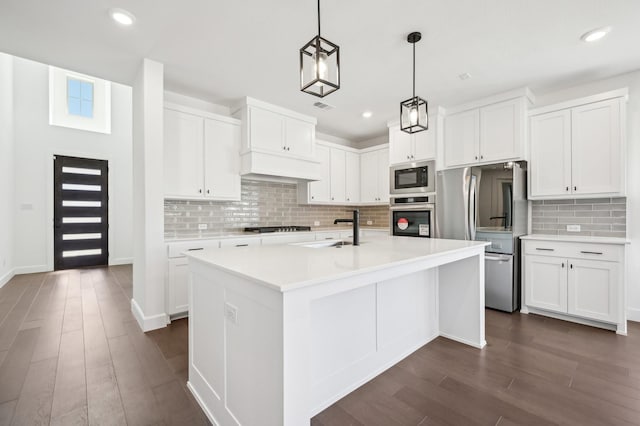 kitchen featuring a center island with sink, decorative light fixtures, stainless steel appliances, light countertops, and white cabinetry