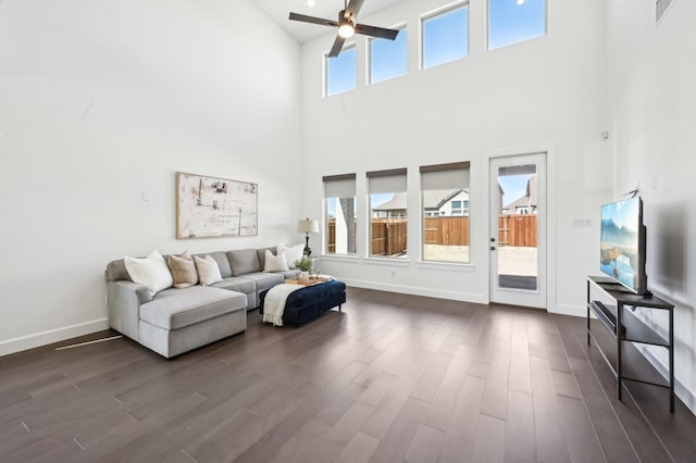 living room with visible vents, baseboards, a ceiling fan, a towering ceiling, and dark wood-type flooring