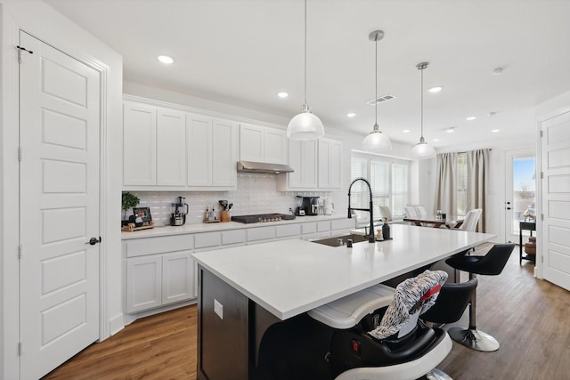 kitchen with gas cooktop, a sink, tasteful backsplash, a center island with sink, and under cabinet range hood