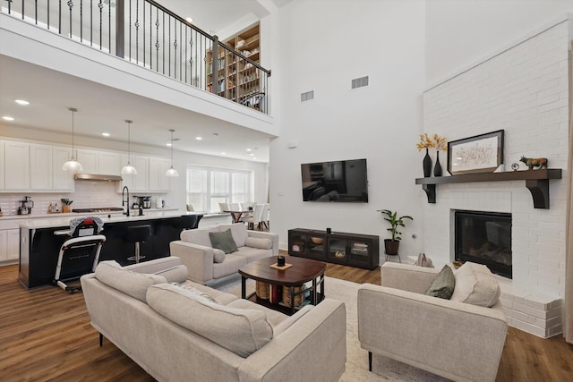 living area featuring visible vents, recessed lighting, a brick fireplace, and dark wood-type flooring