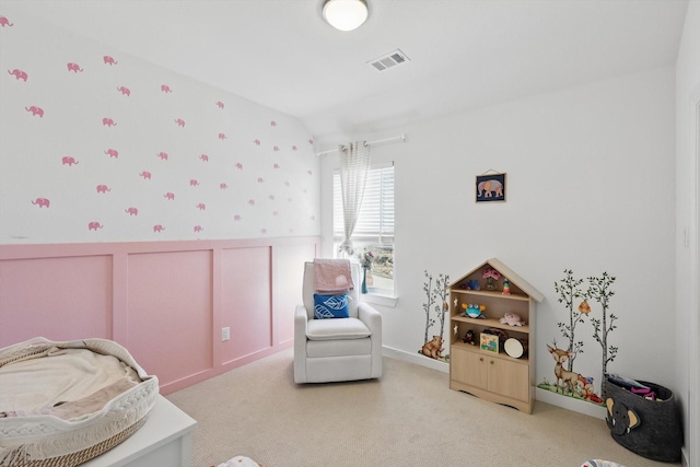 carpeted bedroom with a wainscoted wall, visible vents, vaulted ceiling, and a decorative wall