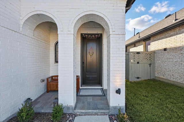 view of exterior entry with brick siding and a gate