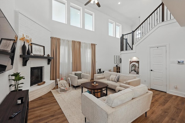 living area featuring ceiling fan, a high ceiling, wood finished floors, and a fireplace