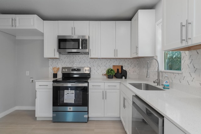 kitchen with light stone counters, stainless steel appliances, decorative backsplash, white cabinetry, and a sink