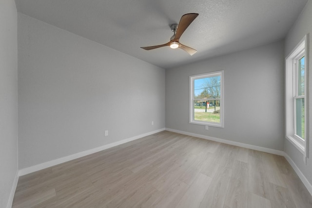 empty room with light wood finished floors, a wealth of natural light, and baseboards