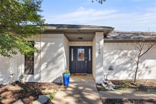 doorway to property with brick siding and roof with shingles