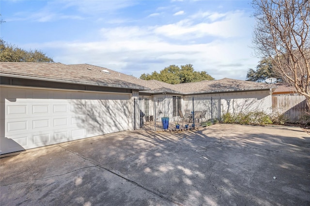 view of side of home with a garage, fence, concrete driveway, and roof with shingles