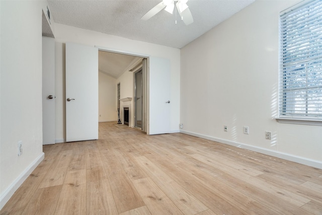 spare room with a textured ceiling, a fireplace, a ceiling fan, baseboards, and light wood-style floors