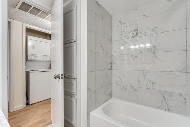 bathroom with stacked washer and clothes dryer, visible vents, shower / tub combination, and wood finished floors