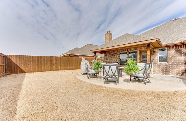 back of house featuring a patio, a fenced backyard, brick siding, roof with shingles, and a chimney