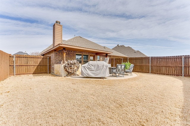 rear view of house with brick siding, a fenced backyard, a chimney, and a patio