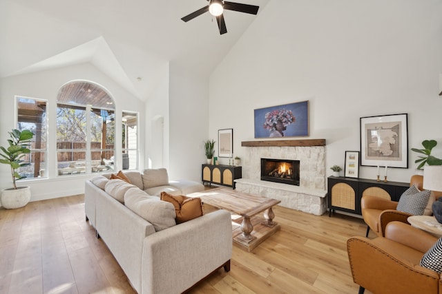 living area featuring light wood-type flooring, high vaulted ceiling, a ceiling fan, and a stone fireplace