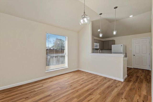 kitchen featuring white appliances, wood finished floors, a peninsula, light countertops, and pendant lighting