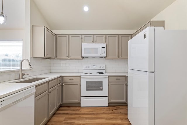 kitchen featuring white appliances, a sink, light wood-type flooring, backsplash, and pendant lighting