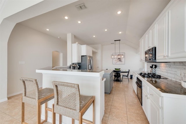 kitchen featuring arched walkways, black appliances, a breakfast bar area, and white cabinetry