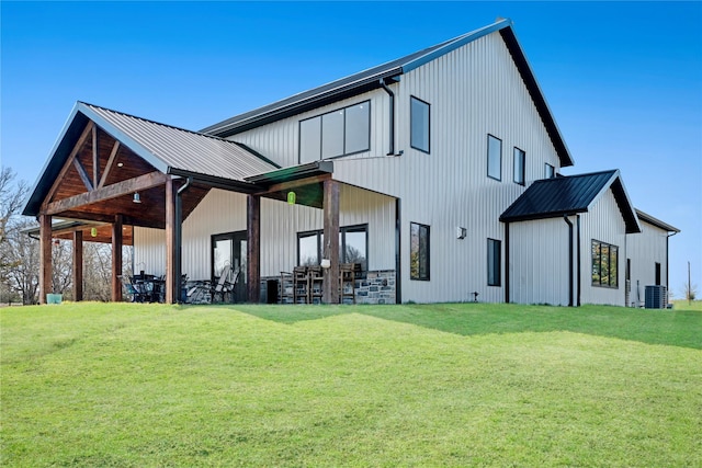 rear view of house featuring cooling unit, metal roof, and a lawn