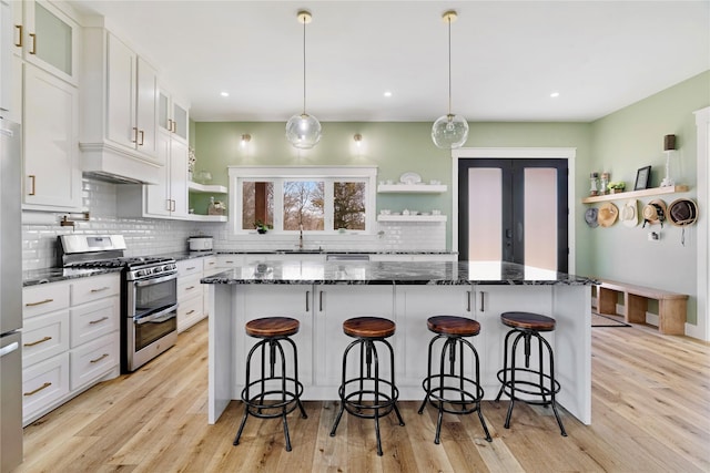 kitchen with dark stone counters, appliances with stainless steel finishes, a breakfast bar area, white cabinetry, and open shelves