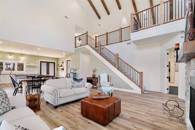 living area featuring beam ceiling, a fireplace, light wood-style floors, baseboards, and stairs