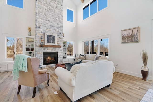 living area featuring light wood-type flooring, baseboards, and a stone fireplace