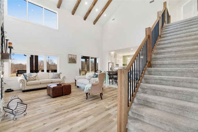 living area with beam ceiling, baseboards, light wood finished floors, and stairs