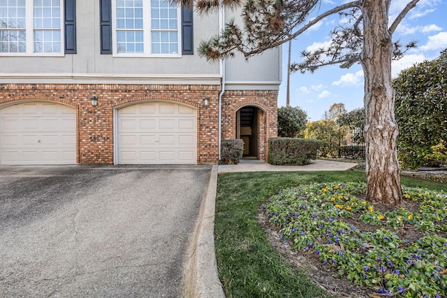 view of front facade featuring aphalt driveway, brick siding, a garage, and stucco siding