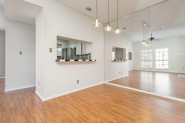 unfurnished living room with ceiling fan, a textured ceiling, visible vents, baseboards, and light wood finished floors