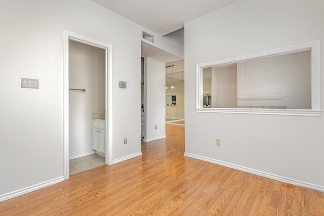 unfurnished room with light wood finished floors, baseboards, visible vents, and a textured ceiling