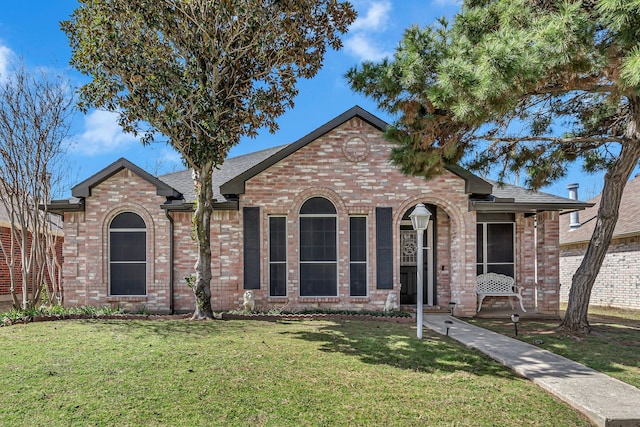 view of front of home featuring brick siding, a front yard, and a shingled roof