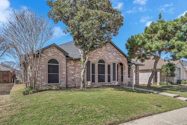 view of front of home with central air condition unit, a shingled roof, a front yard, and brick siding