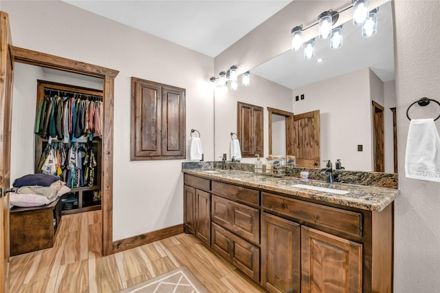 bathroom with a spacious closet, double vanity, a sink, and baseboards