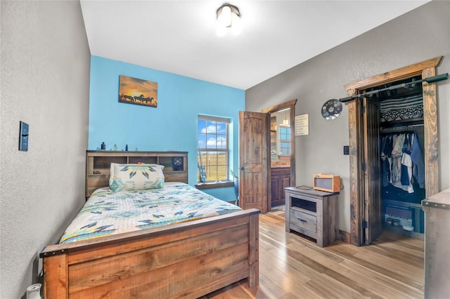 bedroom featuring a textured wall, a closet, ensuite bath, and light wood-style floors