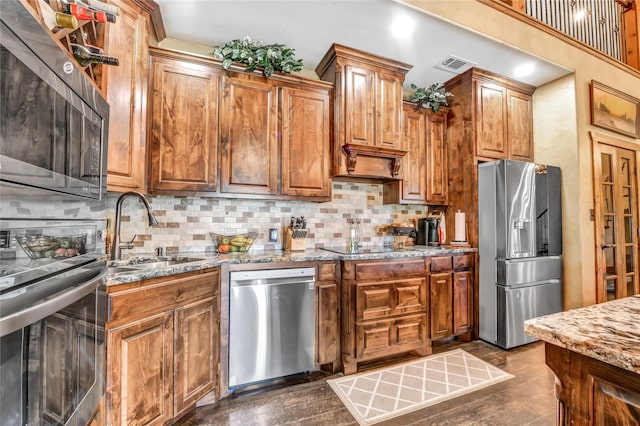 kitchen with stainless steel appliances, a sink, light stone counters, and tasteful backsplash