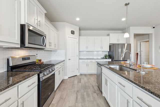 kitchen featuring appliances with stainless steel finishes, white cabinets, decorative light fixtures, and a sink