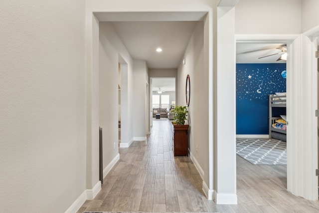 corridor featuring light wood finished floors, an accent wall, and baseboards