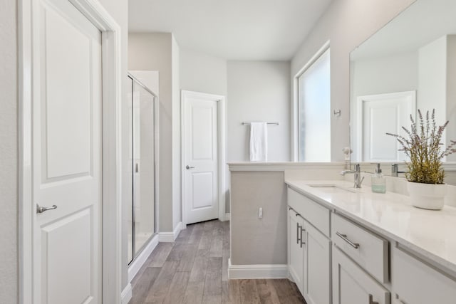 bathroom with baseboards, wood finished floors, vanity, and a shower stall