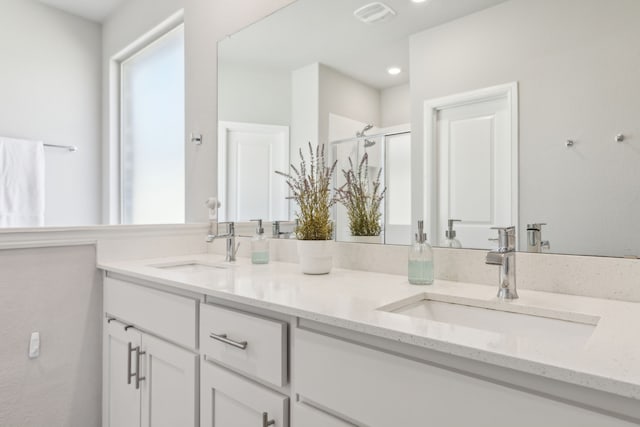 bathroom featuring visible vents, a sink, a shower stall, and double vanity