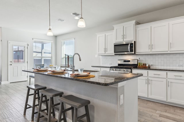 kitchen with appliances with stainless steel finishes, white cabinets, a kitchen island with sink, and hanging light fixtures