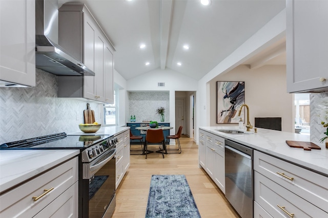 kitchen with lofted ceiling with beams, light wood-style flooring, a sink, wall chimney range hood, and appliances with stainless steel finishes