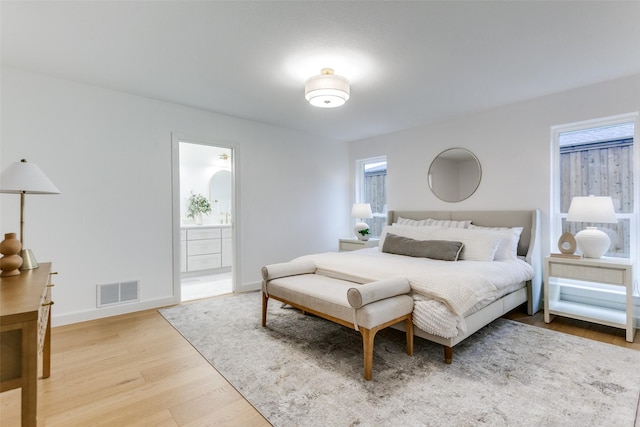 bedroom featuring connected bathroom, wood finished floors, visible vents, and baseboards