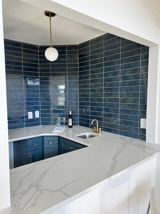 kitchen featuring light stone counters, a sink, tile walls, blue cabinetry, and decorative light fixtures